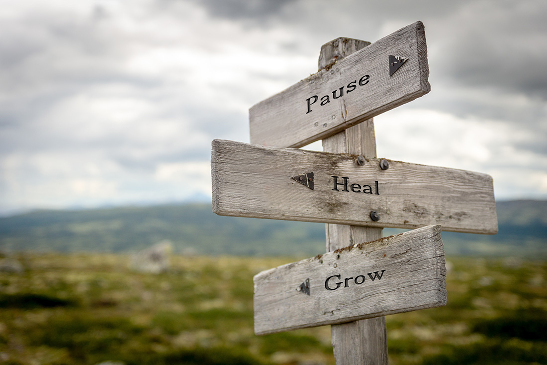 This is a picture of a 3 way wooden road sign which says pause, heal, grow